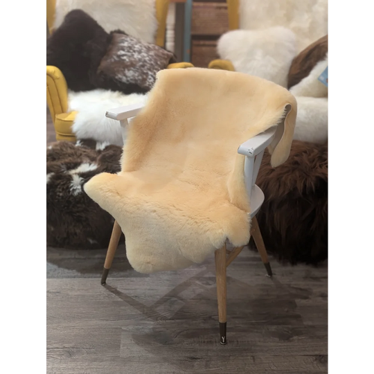 A cozy cream medical sheepskin cover draped over a white wooden chair with light wood legs by angus oliver