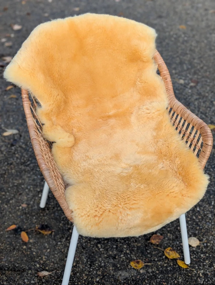 Warm golden yellow medical sheepskin rug draped over wicker chair by angus oliver washable medical sheepskins