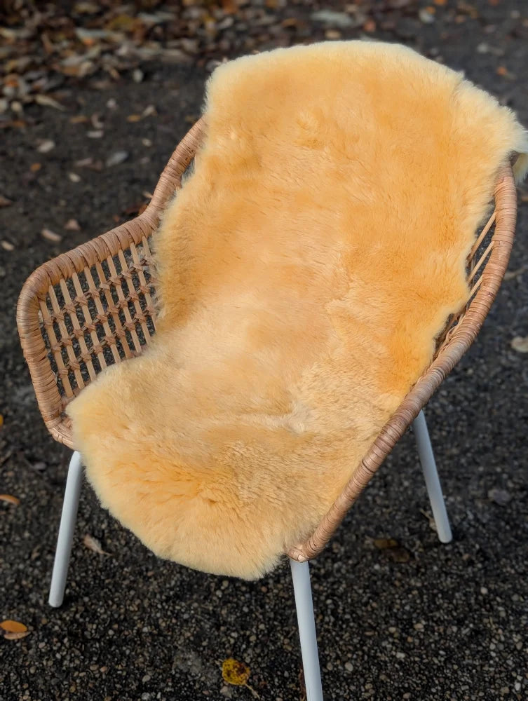 A soft golden-orange washable medical sheepskin rug draped over a wicker chair by angus oliver british sheepskins