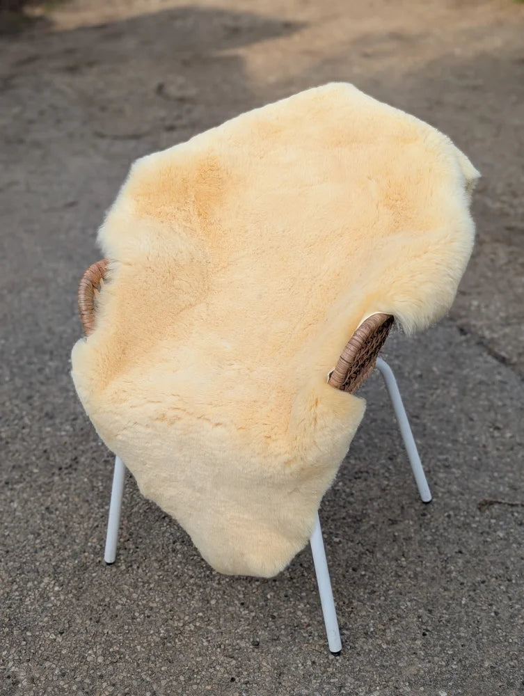 Cream-colored medical sheepskin draped over white metal chair with woven wicker armrests extra large washable medical sheepskins