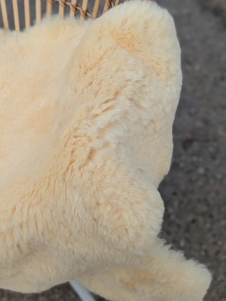 Cream-colored plush medical sheepskin throw draped over a woven chair extra large washable and naturally spotted