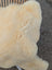Cream-colored plush medical sheepskin throw draped over a woven chair extra large washable and naturally spotted