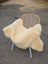 Cream-colored extra large washable medical sheepskin throw draped over woven rattan chair with white metal legs
