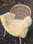 Cream-colored naturally spotted medical sheepskin throw draped over woven wicker chair with white metal legs