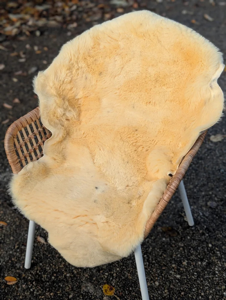 Cream-colored naturally spotted medical sheepskin rug draped over wicker chair washable and soft medical sheepskins