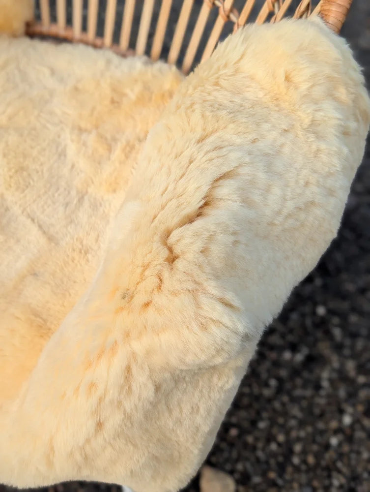 Cream-colored naturally spotted medical sheepskin rug draped over wicker chair washable 45 x 29 inches