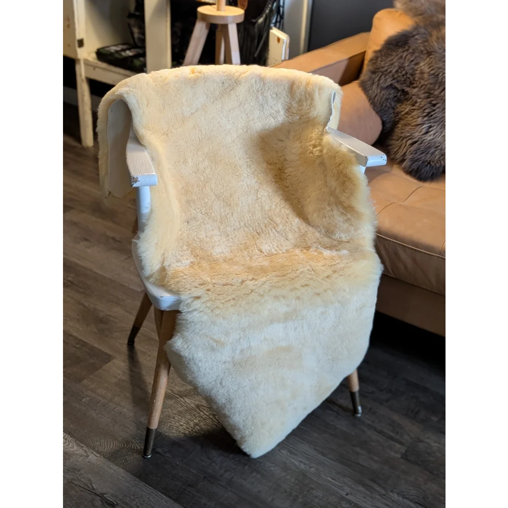 Cream-colored extra large medical sheepskin throw draped over white wooden chair by angus oliver