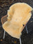 Cream-colored medical sheepskin naturally spotted washable rug draped over a wicker chair for comfort and support