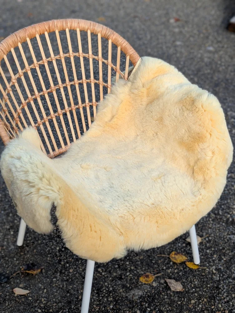 A cozy cream-colored naturally spotted medical sheepskin chair cover draped over a wicker framed chair with white legs
