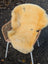 A soft pale yellow medical sheepskin rug with natural spots on a wicker chair from angus oliver british sheepskins