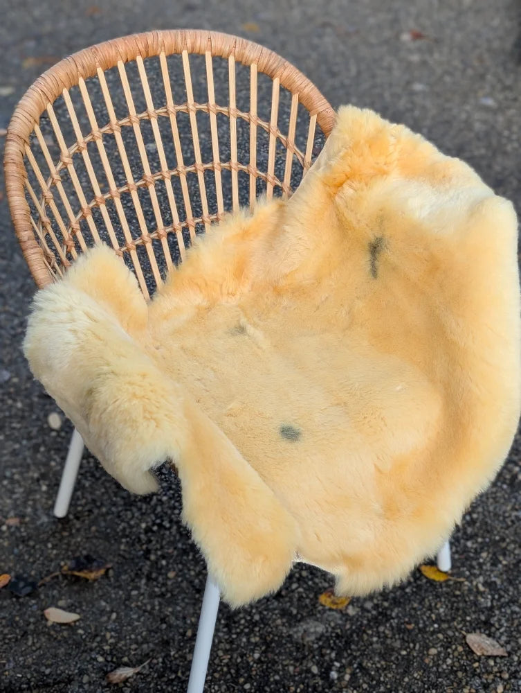 A pale yellow washable medical sheepskin blanket draped over a wicker chair by angus oliver