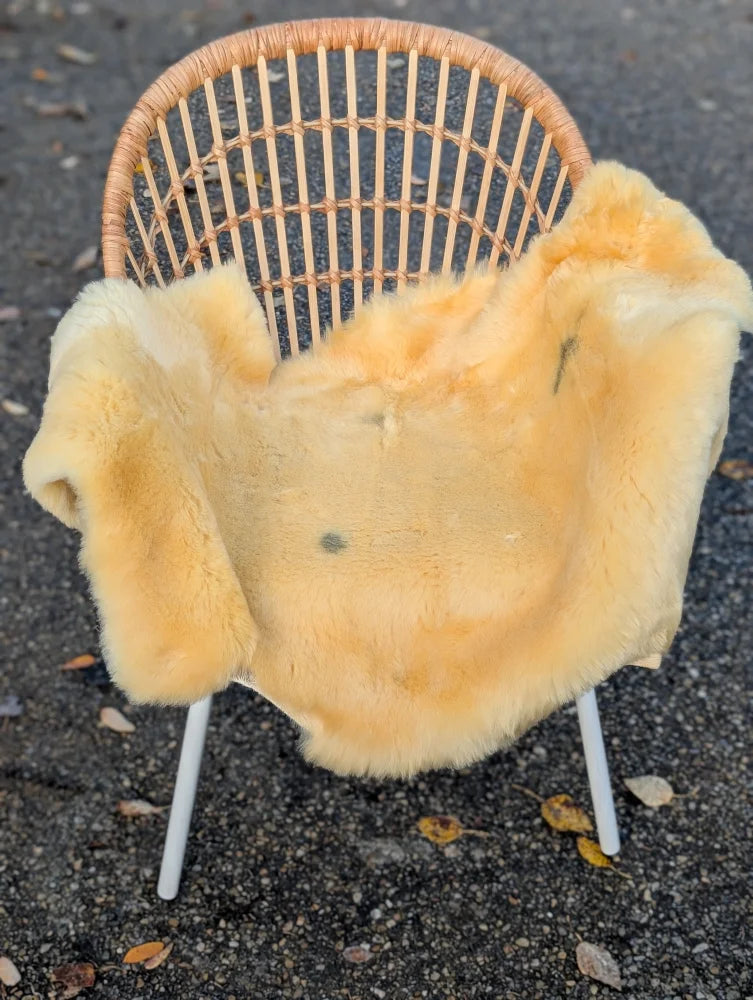A soft pale yellow medical sheepskin blanket draped on a woven wicker chair by angus oliver medical sheepskins