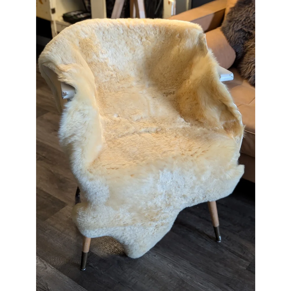 Cream-colored extra large medical sheepskin draped over modern armchair with wooden legs by angus oliver