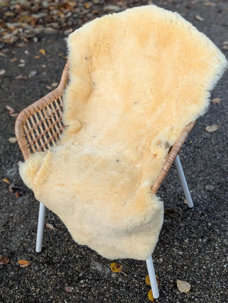 Cream-colored washable medical sheepskin rug draped over wicker chair with white metal legs for comfort and care