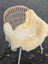 A cozy cream-colored washable medical sheepskin draped over a wicker chair with white metal legs