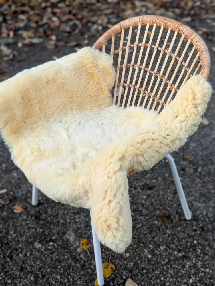 Cream-colored medical sheepskin draped over a woven wicker chair with white metal legs, washable and 49 x 25 inches