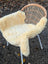 Cream-colored medical sheepskin draped over a woven wicker chair with white metal legs, washable and 49 x 25 inches