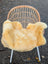 A soft golden-yellow washable medical sheepskin draped over a wicker chair from angus oliver medical sheepskins