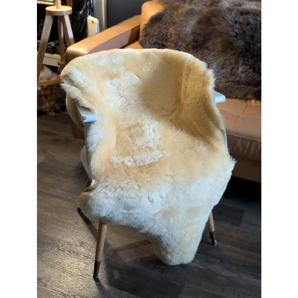 Cream-colored medical sheepskin blanket draped over modern chair with slender wooden legs by angus oliver