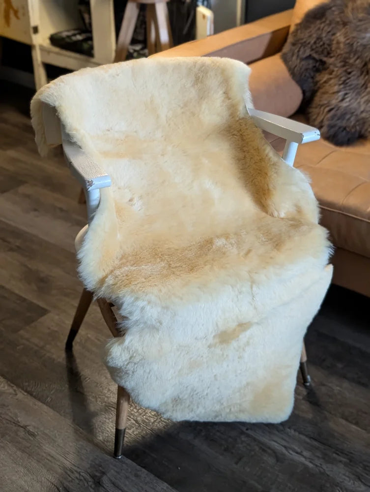 Cream-colored extra large medical sheepskin throw draped over white wooden chair with tapered legs by angus oliver