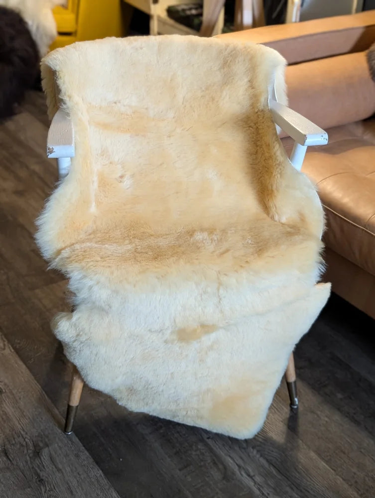 Cream-colored extra large medical sheepskin throw draped over white wooden chair with metal legs by angus oliver