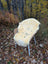 Cream-colored naturally spotted medical sheepskin rug draped over wicker chair on autumn leaves washable medical sheepskins