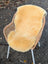 A soft creamy beige medical sheepskin cushion draped over a woven wicker chair by angus oliver british sheepskins