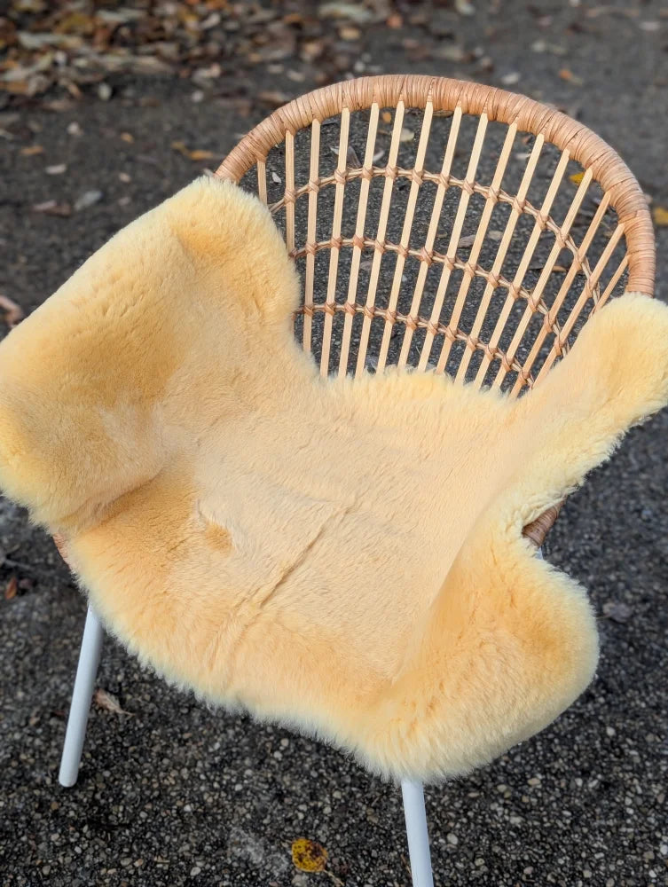 Cream-colored washable medical sheepskin cover draped over wicker chair by angus oliver in medium size