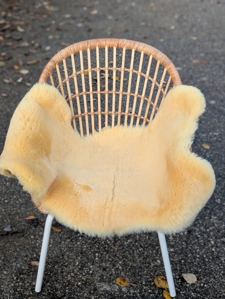 A cozy pale yellow washable medical sheepskin blanket draped over a modern rattan chair by angus oliver british sheepskins