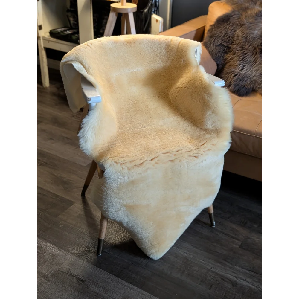 Cream-colored medium medical sheepskin throw draped over modern armchair with slender wooden legs by angus oliver