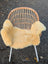 A cozy light beige washable medical sheepskin draped over a wicker chair by angus oliver british sheepskins