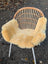 A cozy light beige washable medical sheepskin cushion on a modern rattan chair by angus oliver british sheepskins