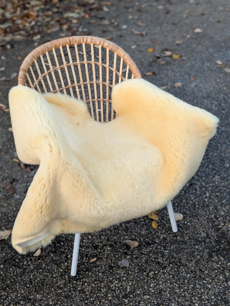 Cream-colored washable medical sheepskin blanket draped over wicker chair with white legs for comfort and care
