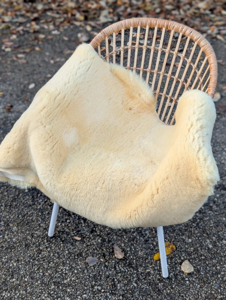 Cream-colored washable medical sheepskin blanket draped over wicker chair featuring soft sheepskin material