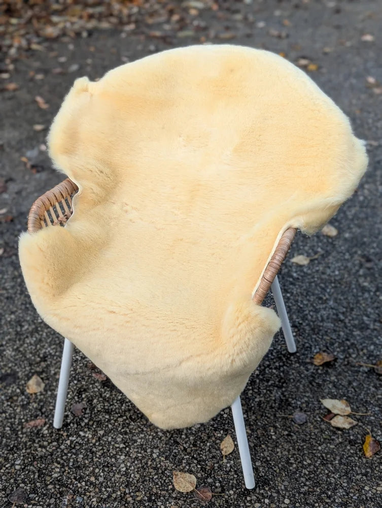 Cream-colored washable medical sheepskin draped over a wicker chair with white legs for comfort and support