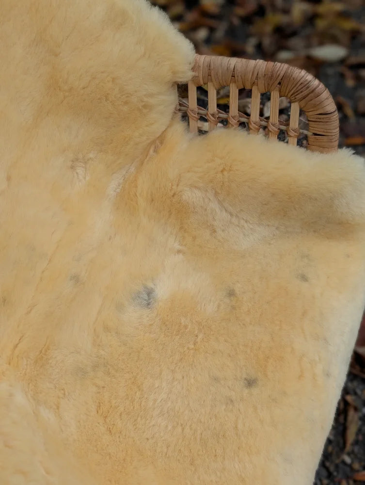 Soft creamy beige medical sheepskin rug with plush natural fur texture and subtle dark spots naturally spotted