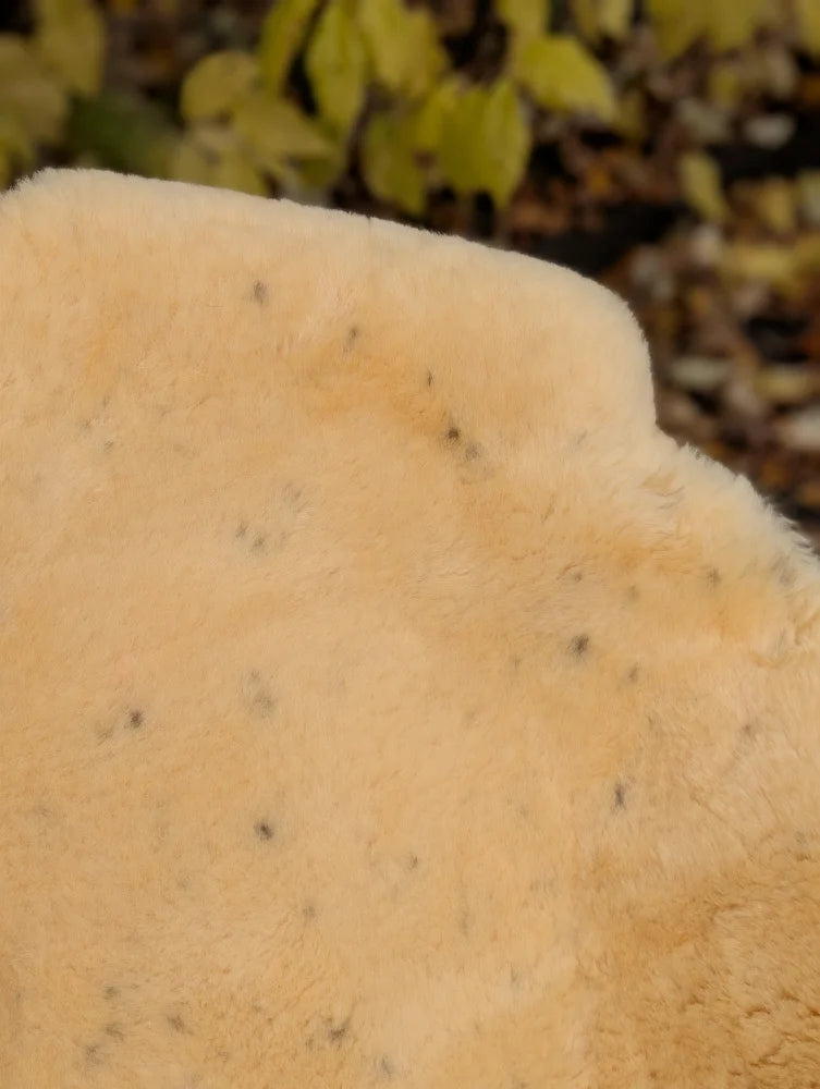Cream-colored plush faux fur medical sheepskin blanket with subtle dark speckles naturally spotted and washable