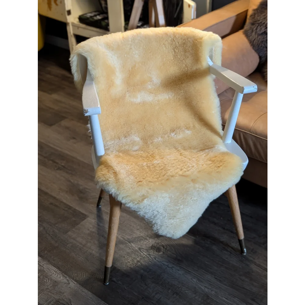 A cozy cream-colored medium medical sheepskin throw draped over a white wooden armchair by angus oliver