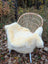 Cream-colored medical sheepskin blanket naturally spotted draped over woven wicker chair with white metal legs