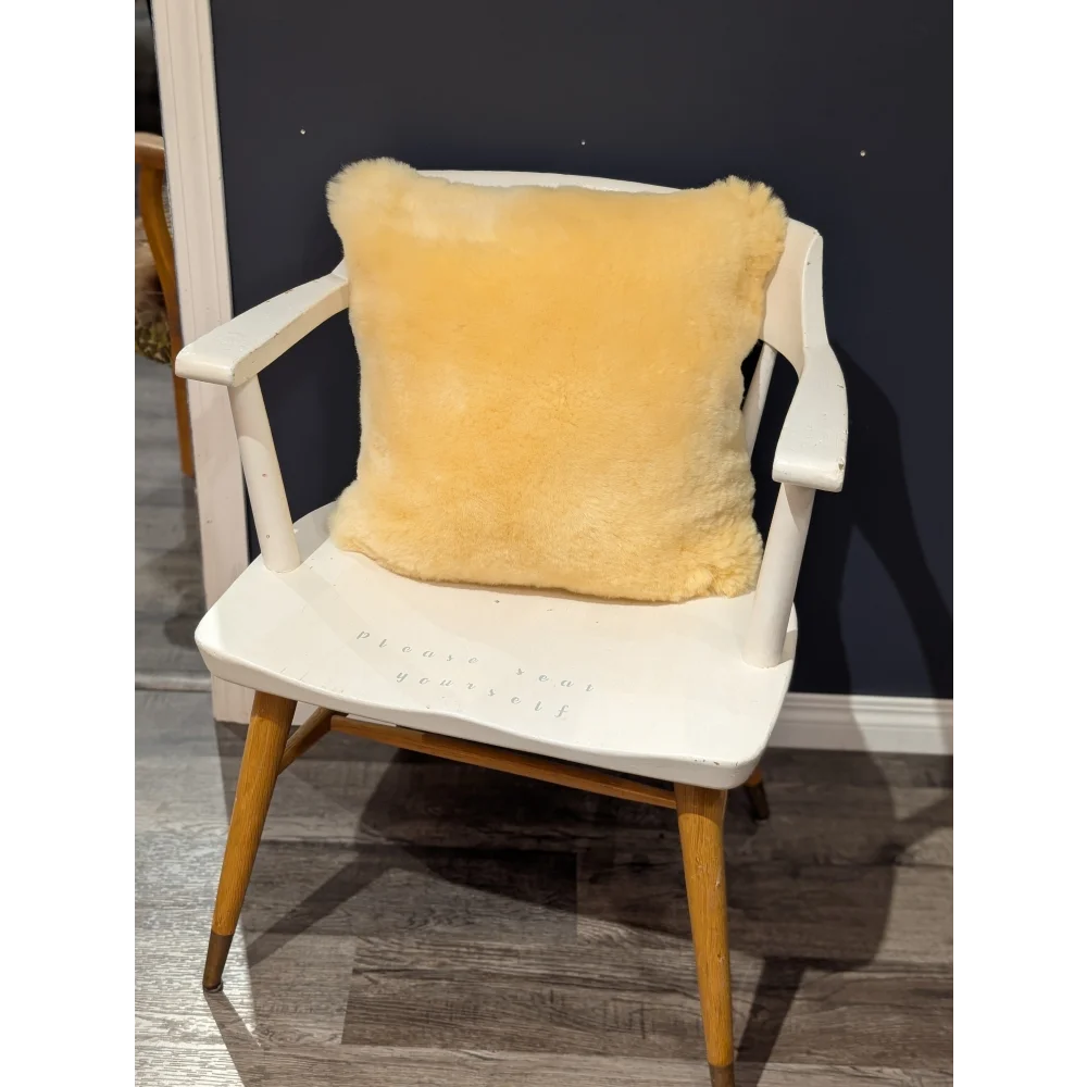 A soft golden-yellow medical sheepskin cushion with plush texture on a white wooden chair with cushion cover