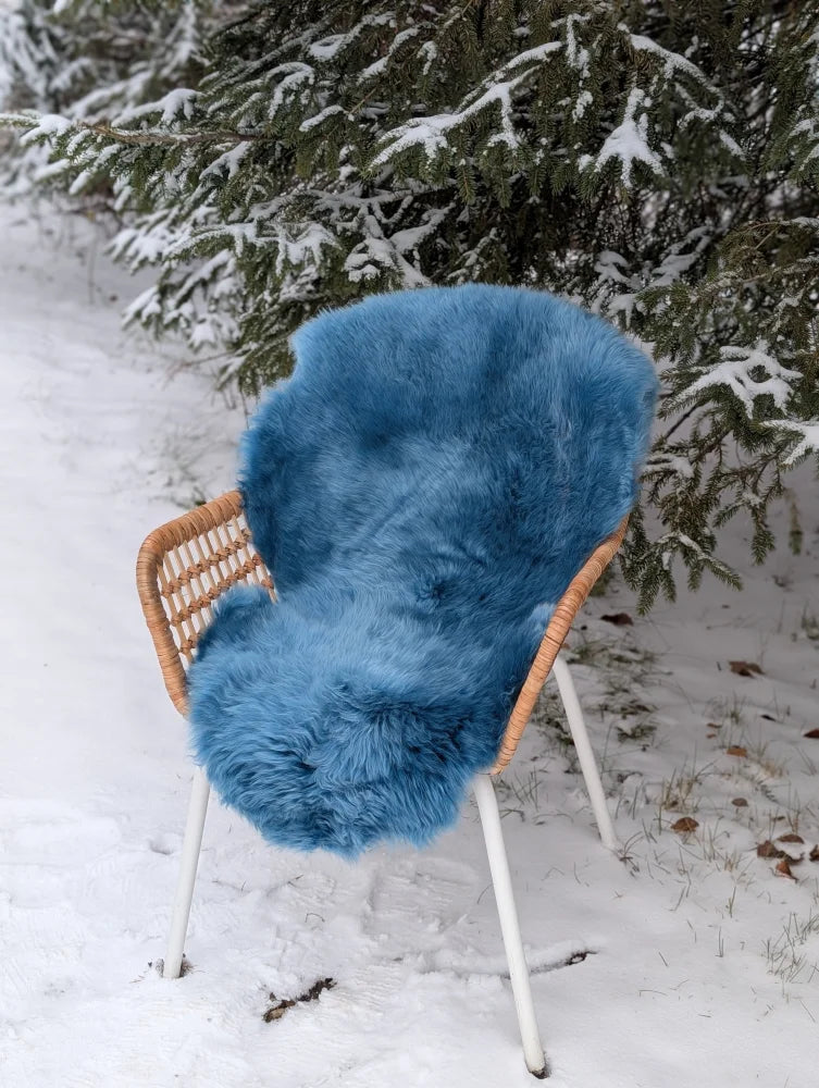 A vibrant blue merino sheepskin rug draped over a wicker chair with white metal legs perfect for mid october decor