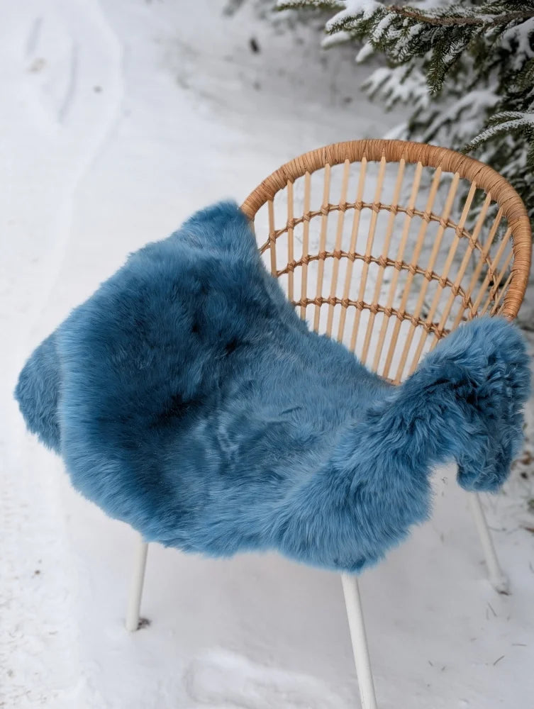 A vibrant blue merino sheepskin throw draped over a woven wicker chair perfect for mid october cozy vibes