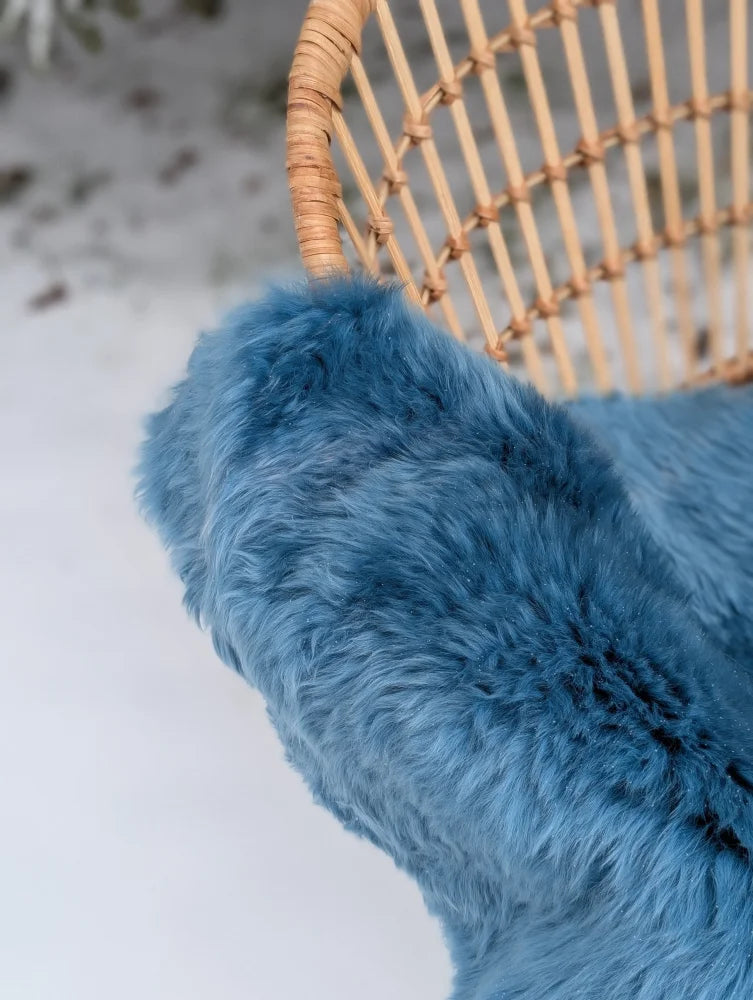 A plush deep blue merino sheepskin throw draped over a wicker chair arm perfect for mid october coziness