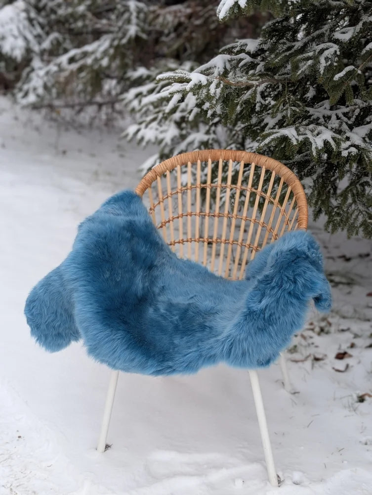 A plush blue merino sheepskin throw draped over a wicker chair with white metal legs perfect for mid october cozy vibes