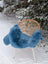 A plush blue merino sheepskin throw draped over a wicker chair with white metal legs perfect for mid october cozy vibes