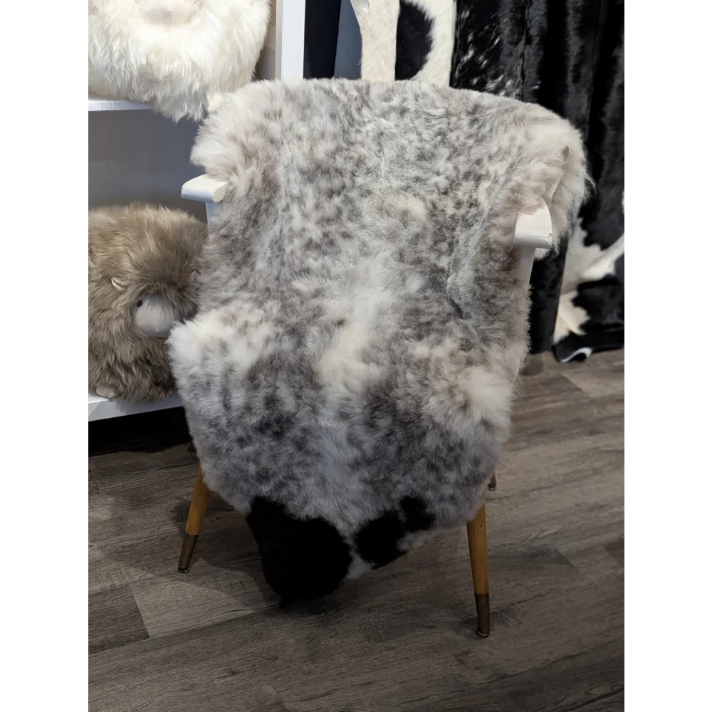 A medium dalmatian icelandic sheepskin rug with short wool draped over a wooden chair with brass legs