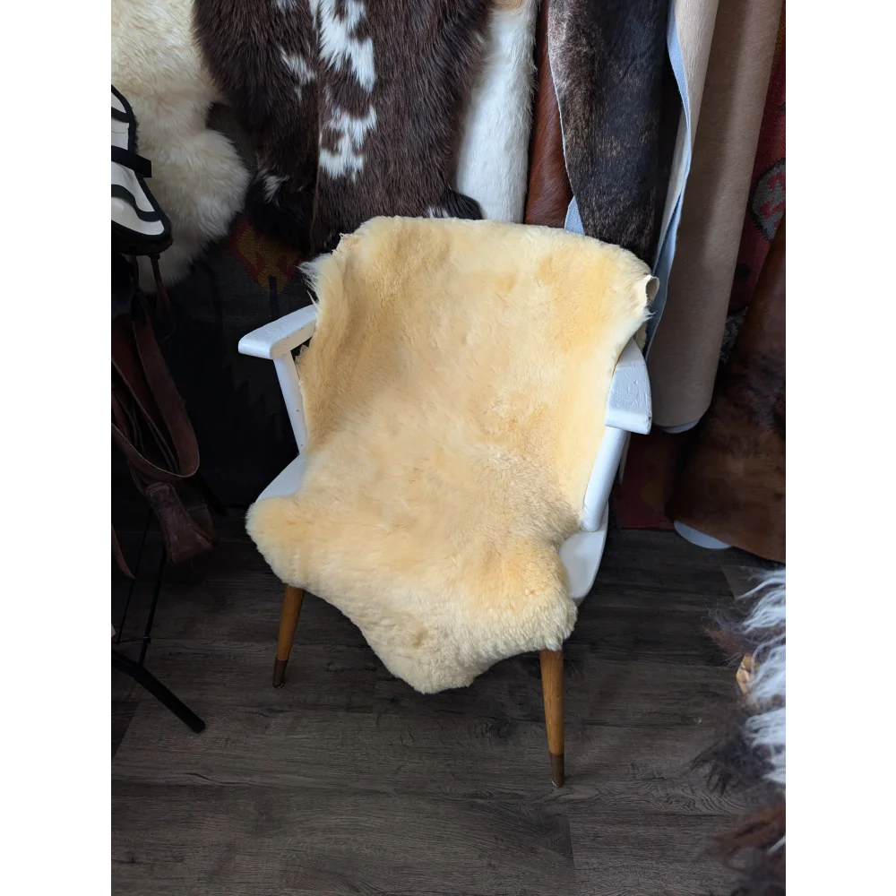 A soft creamy yellow medium medical sheepskin rug draped over a white wooden chair by angus oliver