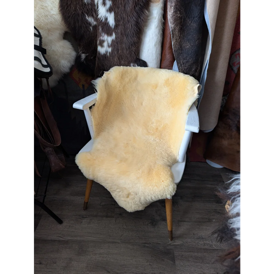 A soft creamy yellow medium medical sheepskin rug draped over a white wooden chair by angus oliver