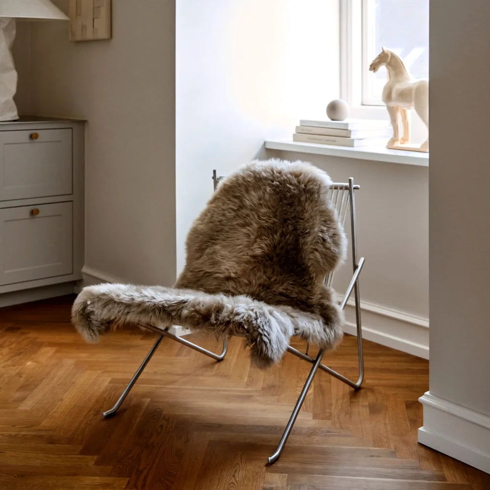 A cozy medium taupe merino sheepskin rug draped over a minimalist chair made from dyed merino sheepskins meeting strict european standards