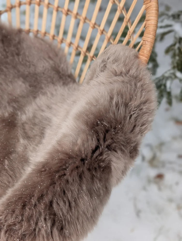 A soft medium taupe merino sheepskin throw draped over a wicker chair arm showcasing its fluffy texture